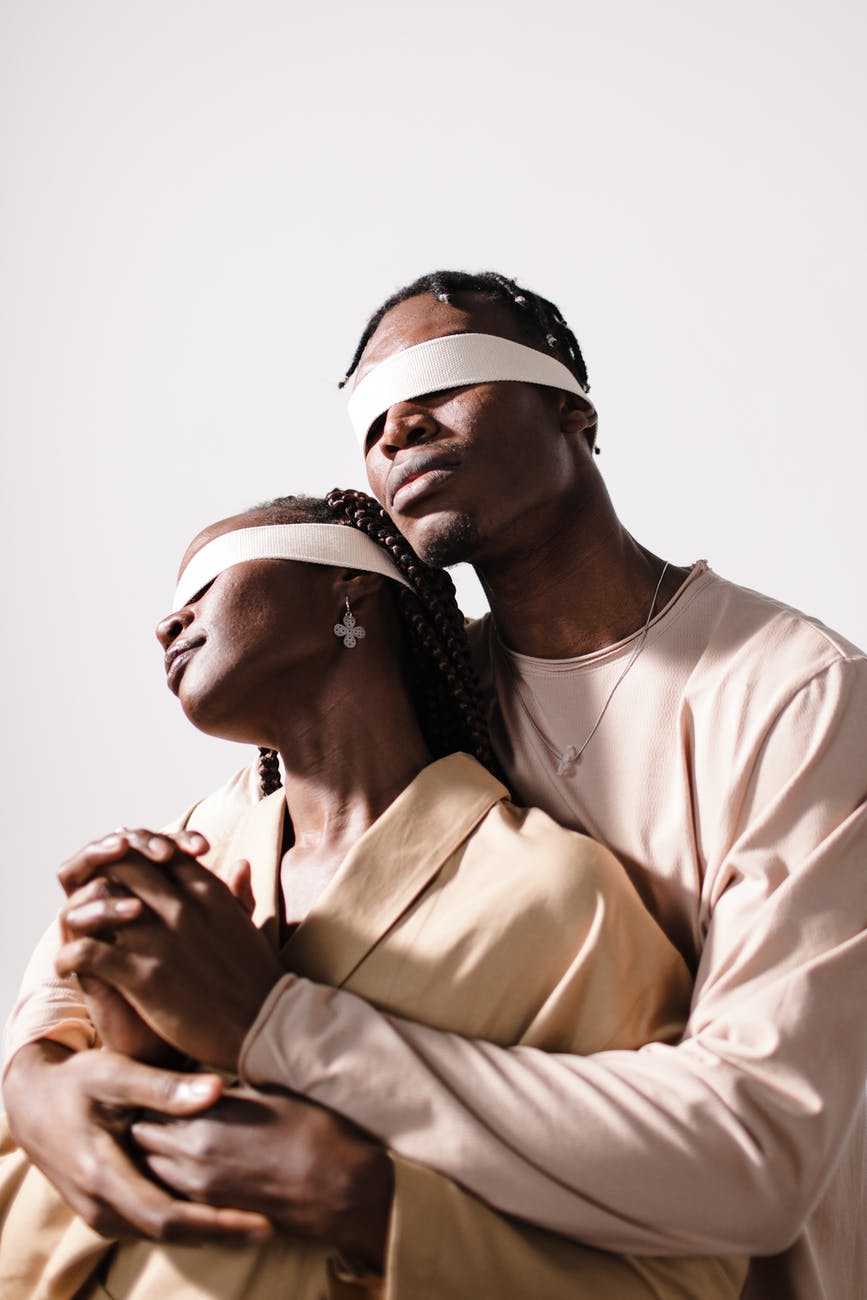 man in beige long sleeves shirt hugging woman wearing brown coat blindfolded